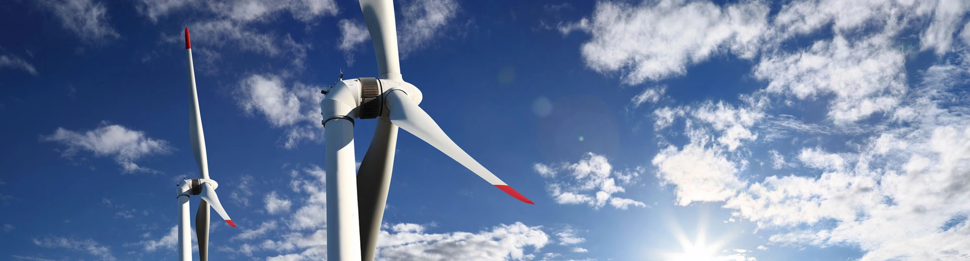 Two wind turbines against a blue sky with scattered clouds and sunlight.