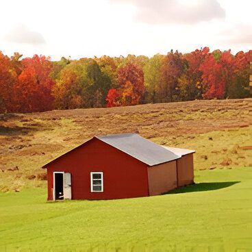 A red barn sits on a grassy field with a backdrop of colorful autumn trees.