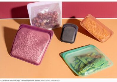 Reusable silicone bags filled with beans, grapes, pasta, and snap peas are arranged against a pink and orange background.