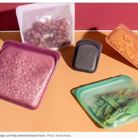 Reusable silicone bags filled with beans, grapes, pasta, and snap peas are arranged against a pink and orange background.